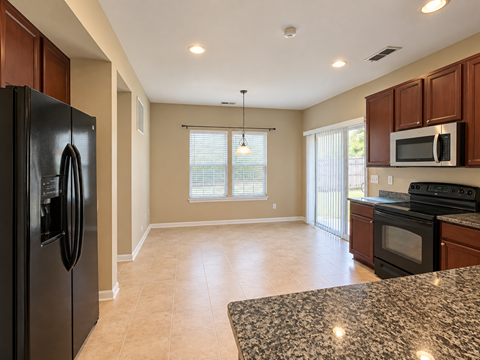 A kitchen with a black fridge and microwave, a black oven, and a granite countertop.