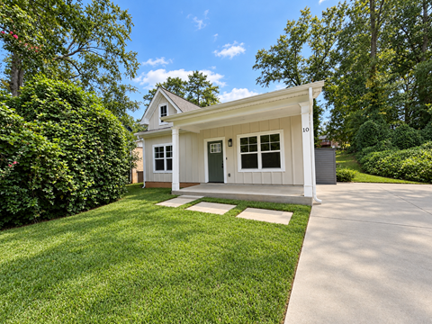 A small white house with a porch and a green lawn in front.