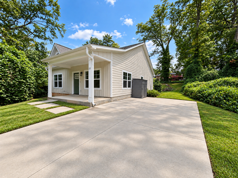 A small white house with a porch and a driveway in front.