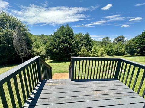 A wooden deck with railings overlooks a grassy area with trees.
