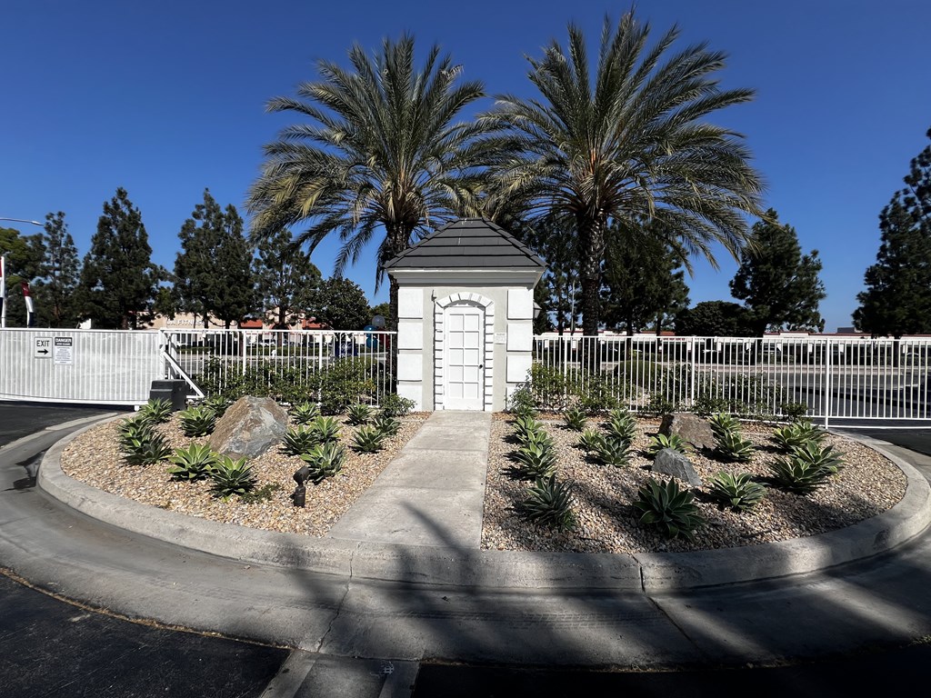 A small white building with a black roof is surrounded by a white fence and palm trees.