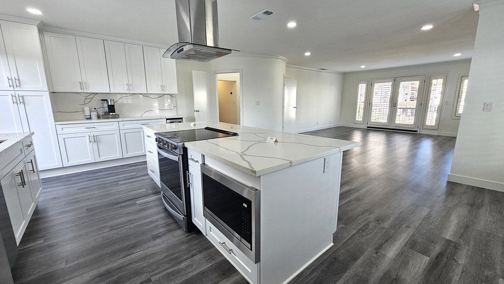 a kitchen with white cabinets and a large island with a stove and a microwave