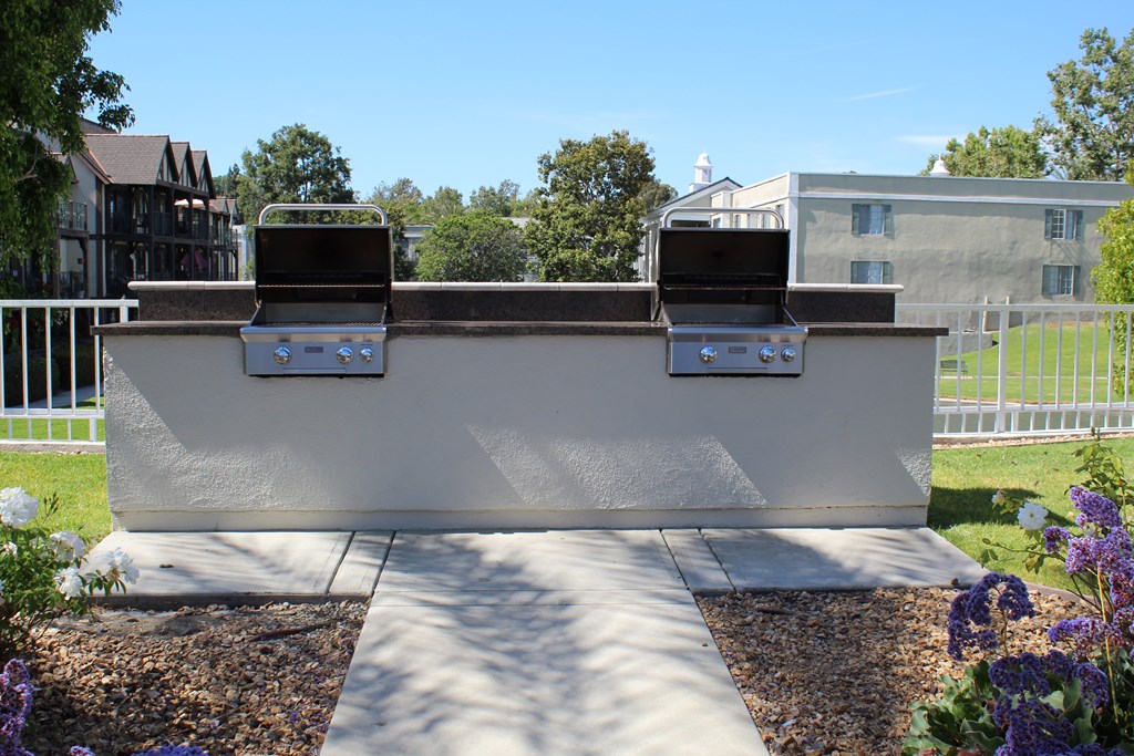 A white outdoor grill with two burners is in the middle of a gravel area.