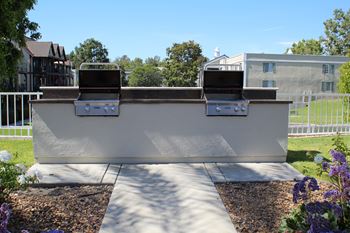 A white outdoor grill with two burners is in the middle of a gravel area.