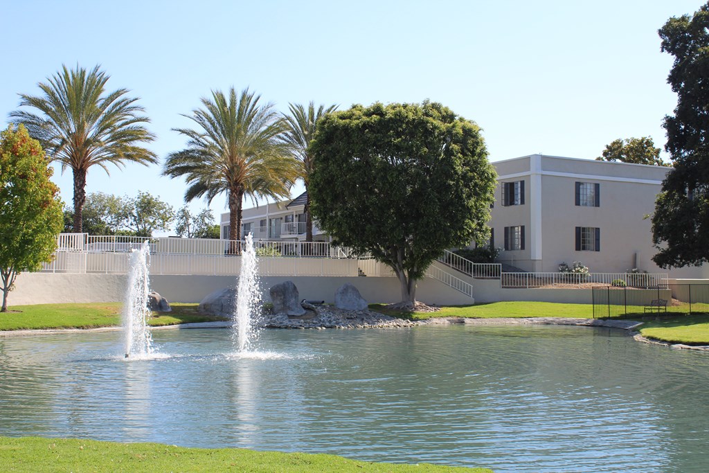 A fountain in the middle of a pond in front of a building.