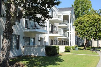 A white apartment building with balconies and trees in front.