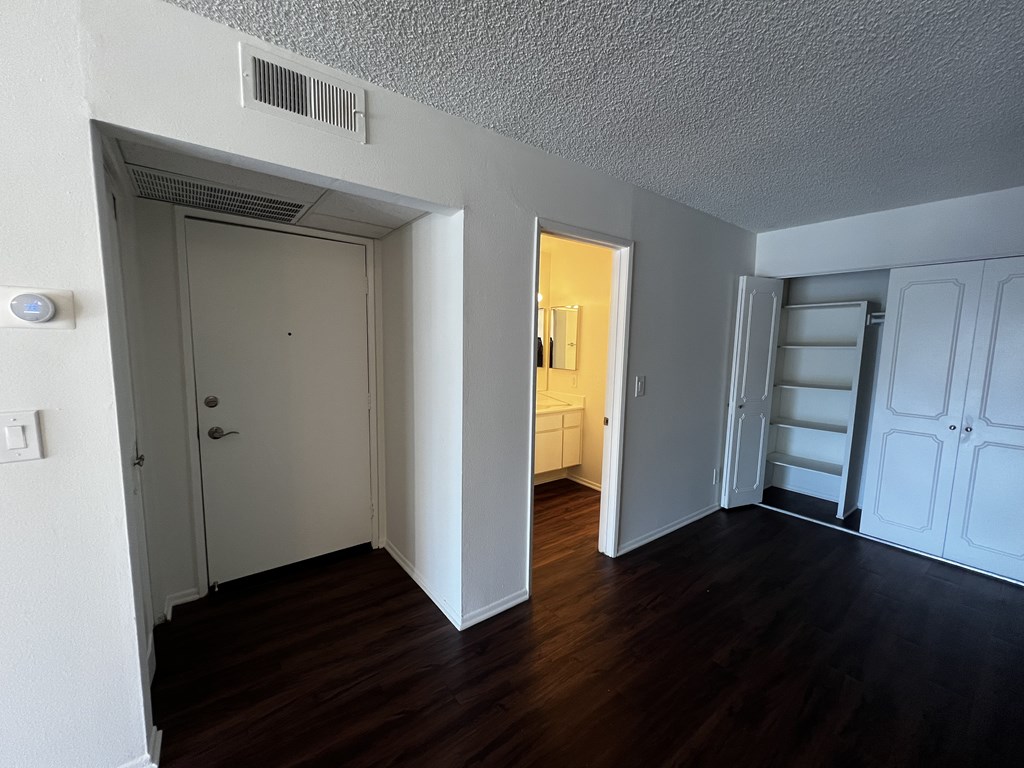 A room with white walls and wooden floors has two doors and a window.