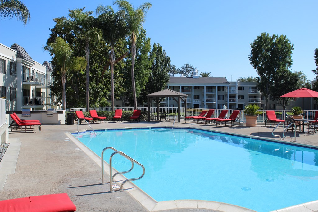 A swimming pool surrounded by red chairs and trees.
