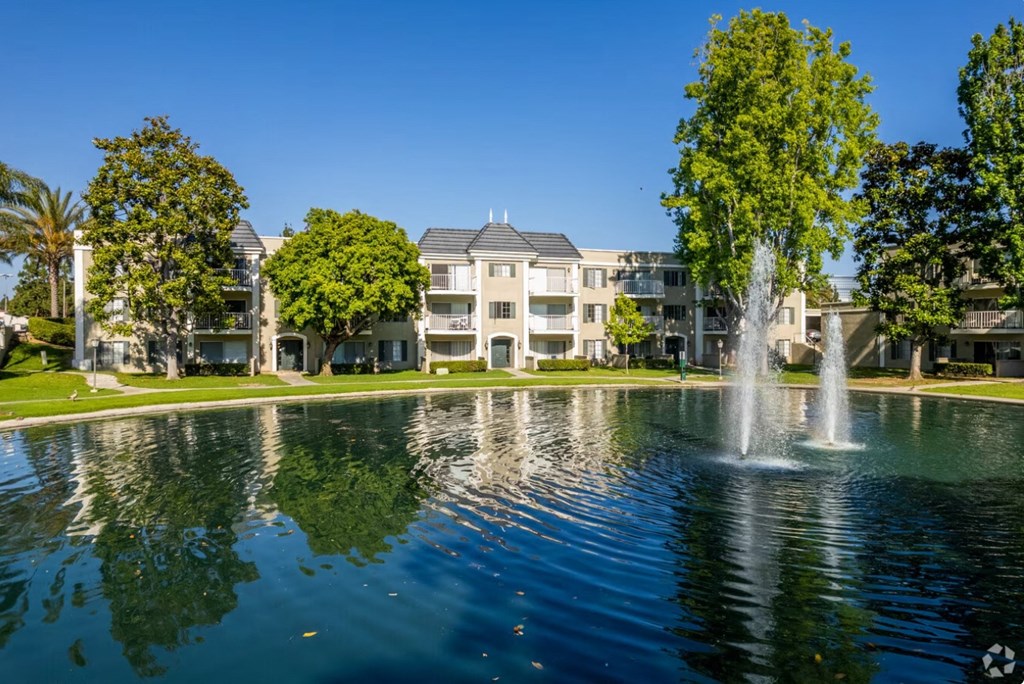 a fountain in the middle of a pond with apartment buildings in the background