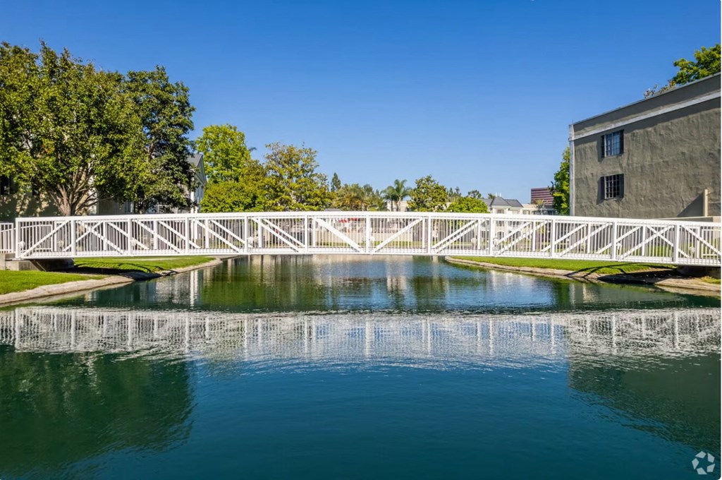 a white bridge crosses a pond in front of a gray building