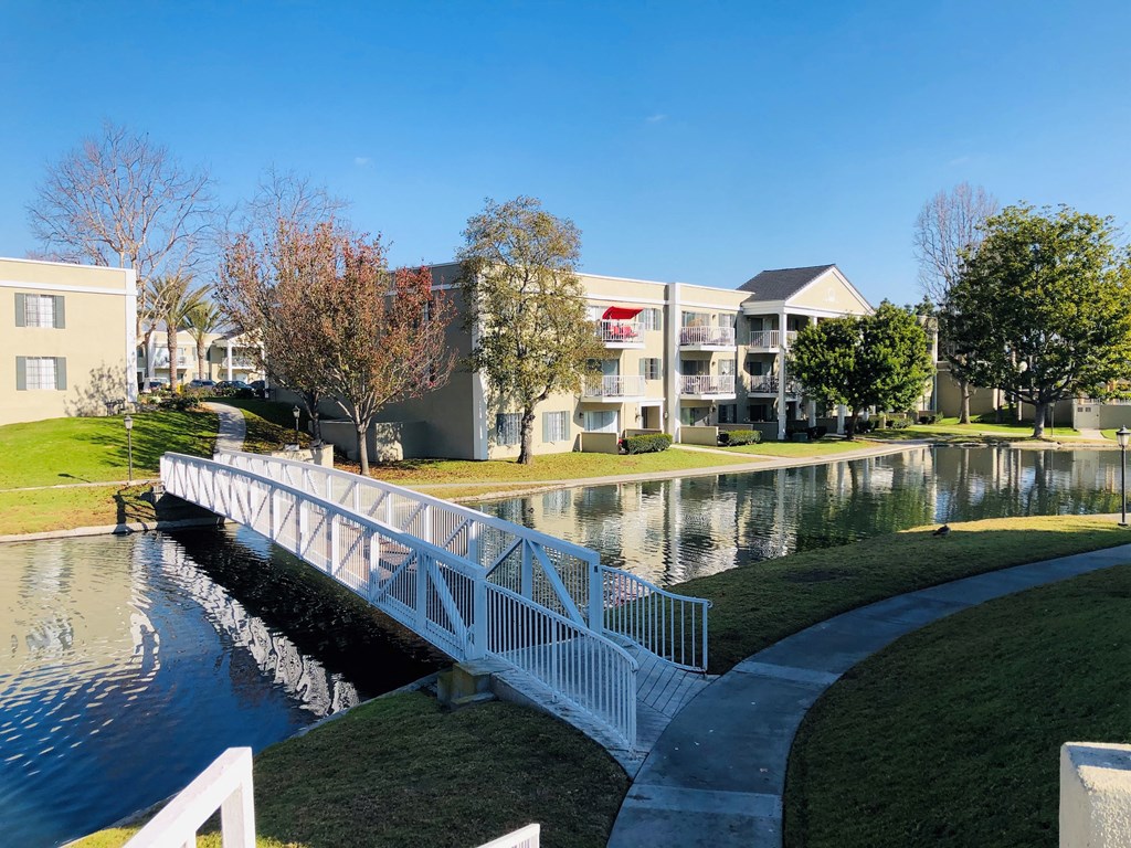 a white bridge over a pond with apartment buildings in the background