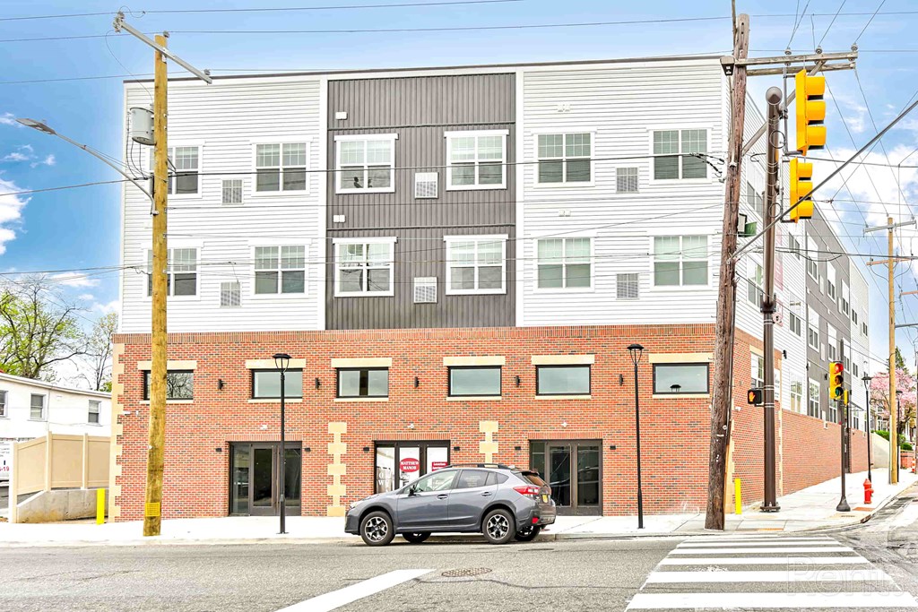 A grey car is parked in front of a building with a yellow sign on the right.