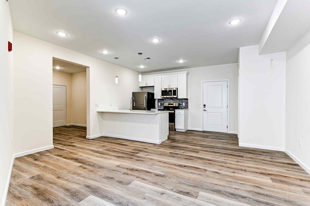A room with a wooden floor and a kitchen area with white cabinets.