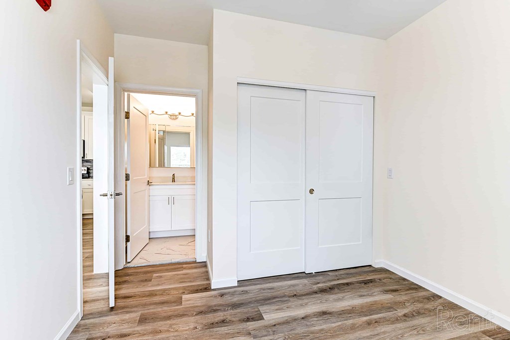 A white door is closed and another is open in a room with wooden flooring.