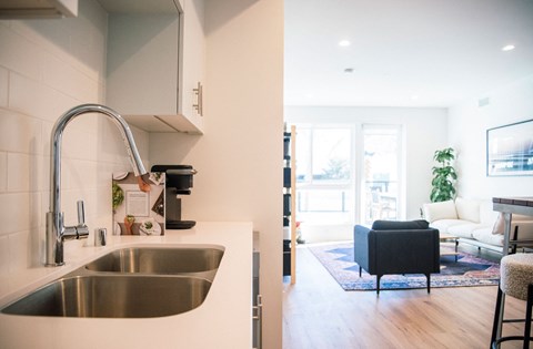 A modern kitchen with a stainless steel sink and a black chair in the living room.