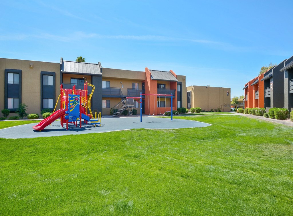 Outdoor, brightly colored playground and swings surrounded by large grassy area for kids to play