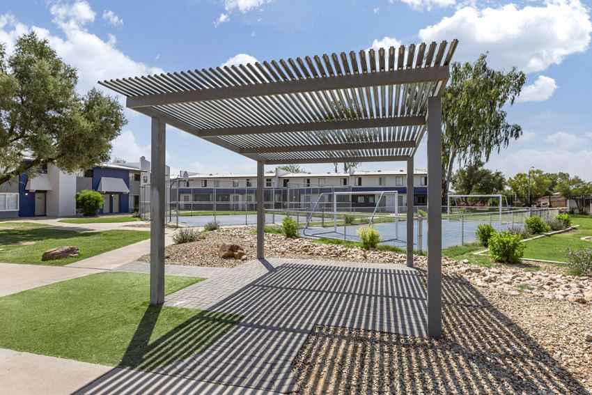 a pergola in front of a tennis court with a building in the background