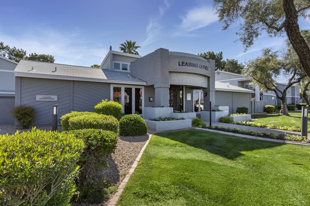 the exterior of a grey building with a lawn and a garden