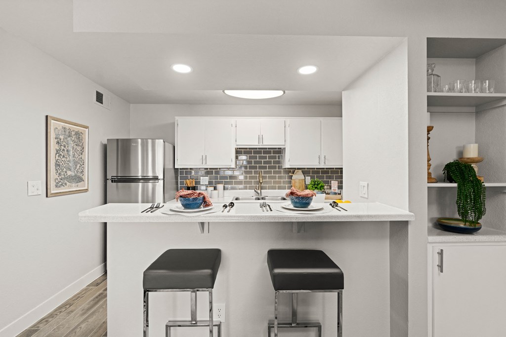 a kitchen with white cabinets and a white counter top with two stools in front of it