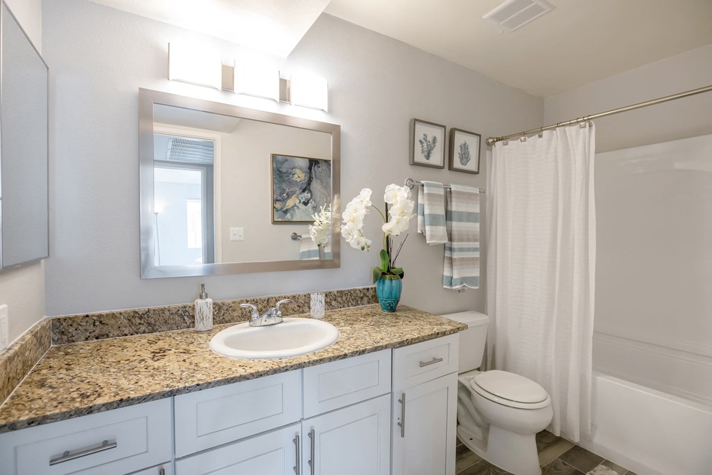 Beautiful bathroom with tile flooring, white cabinetry, and white tub and sink with a large mirror