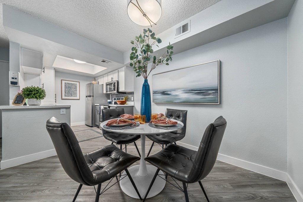 a dining area with a table and chairs and a kitchen in the background