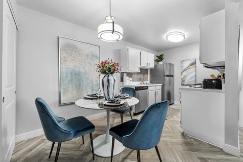 a dining area with a table and four chairs and a kitchen in the background