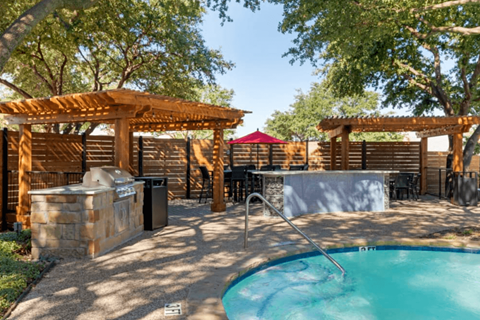 A pool area with a wooden pergola and a stone fountain.