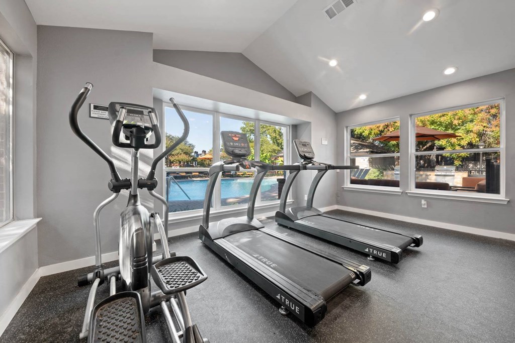 the gym is equipped with cardio equipment and a view of the pool