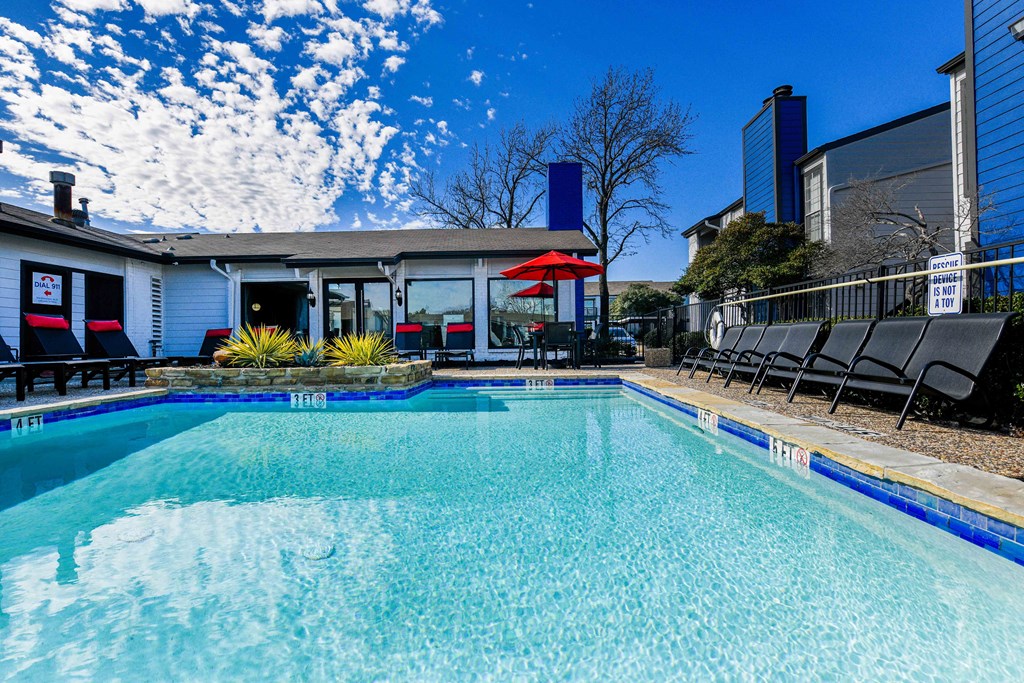 a swimming pool with chairs and a building in the background