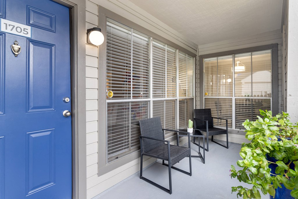 the front porch of a house with chairs and a table and a blue door