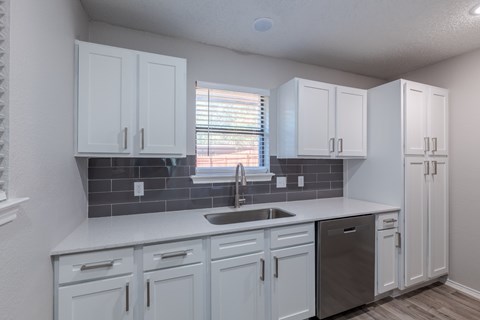 A kitchen with white cabinets and a grey backsplash.