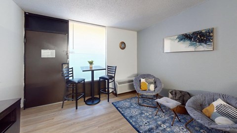 A living room with a grey couch, a table with four chairs, and a blue rug.