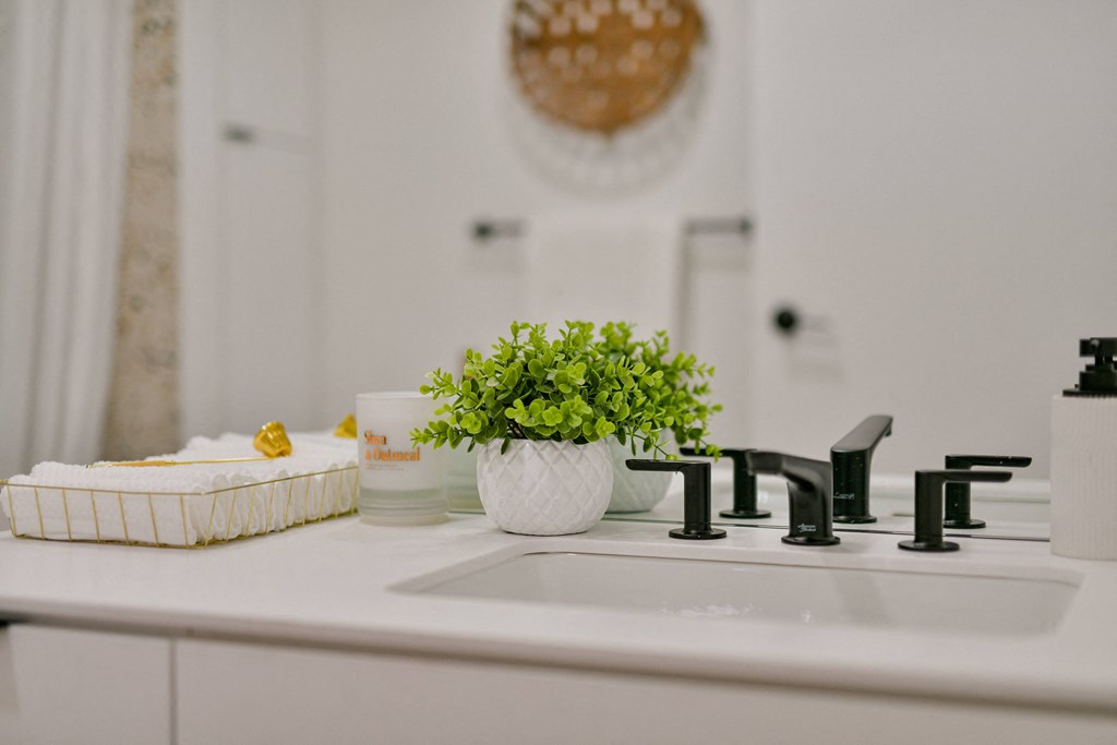 a white bathroom with a sink and a vase with a plant