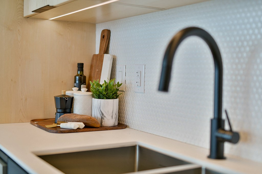 a kitchen sink with a black faucet and a wooden tray with kitchen implements