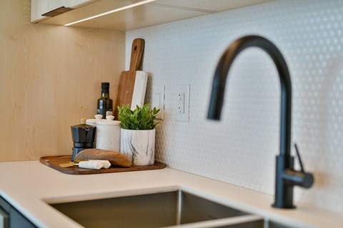 a kitchen sink with a black faucet and a wooden tray with kitchen implements