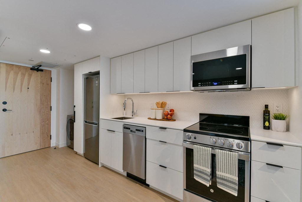 a kitchen with white cabinetry and stainless steel appliances and a television