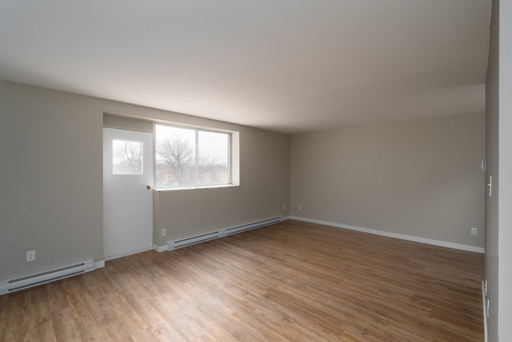 an empty bedroom with a large window and hardwood floors
