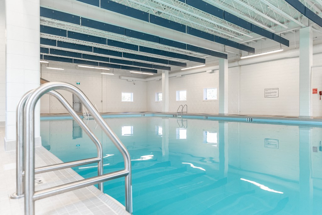 a large indoor swimming pool with white tiles and a stainless steel handrail