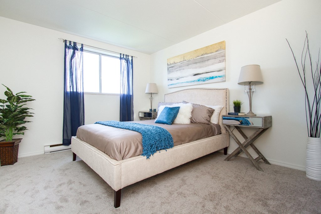 a bedroom with white walls and a beige bed with blue and brown pillows