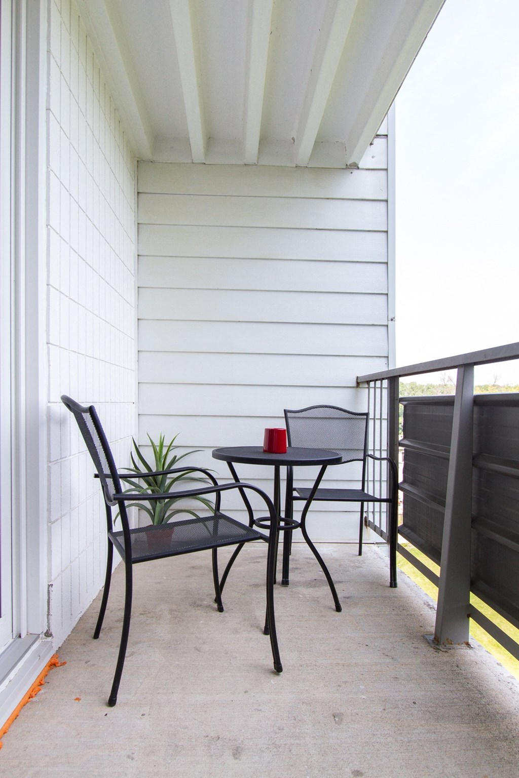 a small patio with two chairs and a small table with a red cup on it