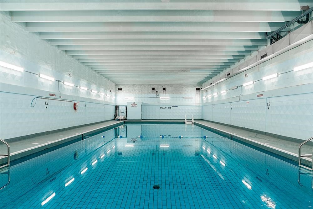 a large swimming pool in a white room with blue tiles