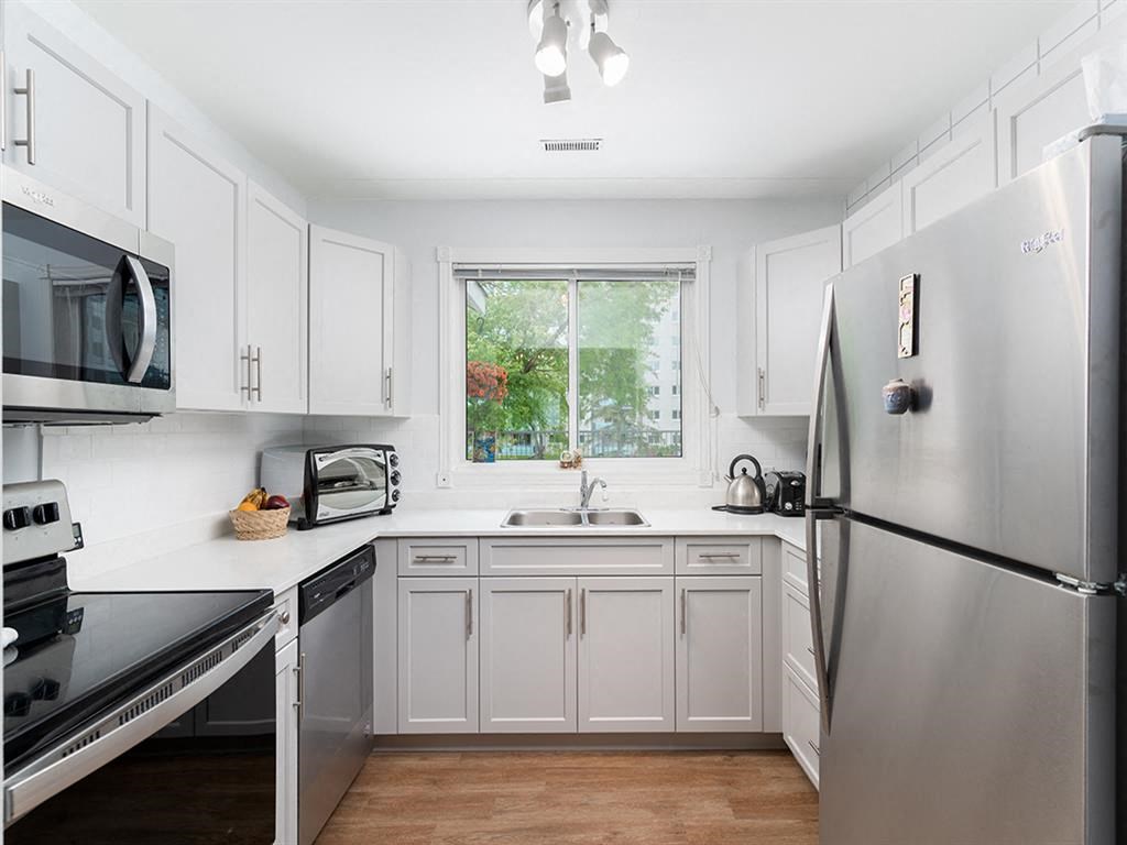 a white kitchen with stainless steel appliances and a window