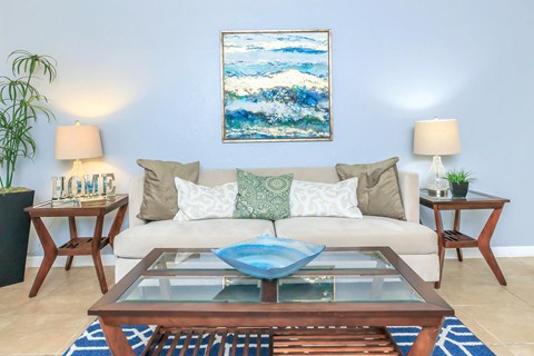 A living room with a white couch, a blue coffee table, and a painting on the wall.