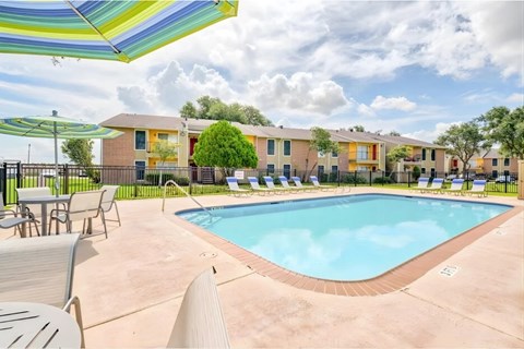 A pool surrounded by chairs and umbrellas in front of apartment buildings.