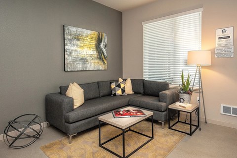 A living room with a grey couch, a coffee table, and a painting on the wall.