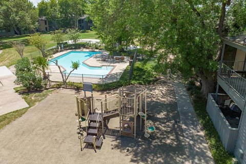 A playground with a slide and swings is surrounded by a fence and a pool.