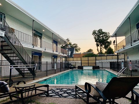 A pool surrounded by a black fence and chairs.