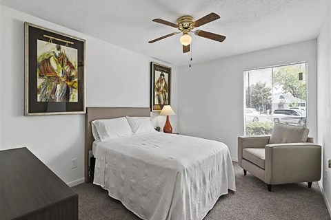 A bedroom with a bed, chair, and two paintings on the wall.