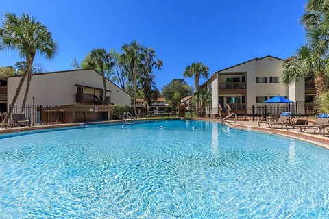 Large swimming pool in front of a building with palm trees.