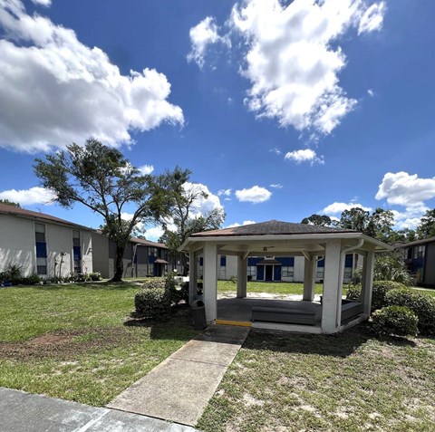 A gazebo is in the middle of a grassy area with apartment buildings in the background.